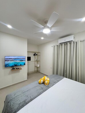 A hotel room with a bed, a ceiling fan, an air conditioning unit, a television, a wall-mounted shelf, a wardrobe, and a curtain. - Orquidea Apt 1- NEW 2 bdr-2bth with pool-perfect retreat (Washington)