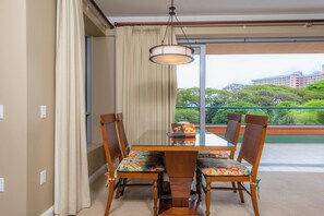 Comedor con mesa y sillas, una lámpara colgante y vistas a zonas verdes y edificios a través de un ventanal amplio.