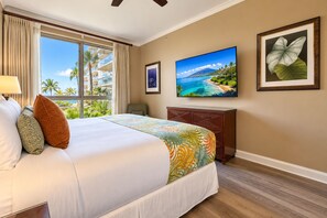 Une chambre d’hôtel avec un grand lit, une télévision, un bureau et une fenêtre donnant sur des palmiers et une plage.