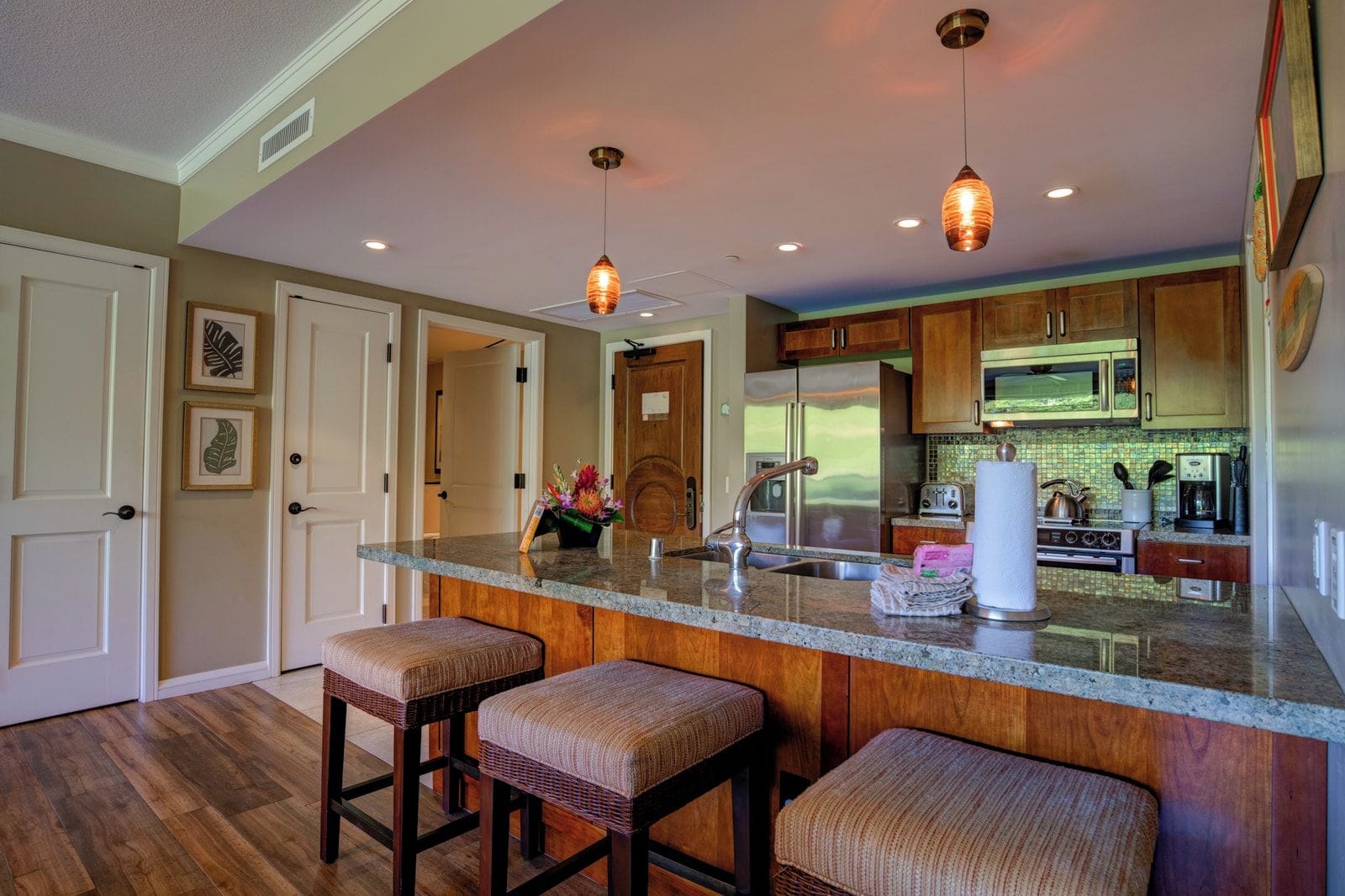 Una cocina con barra, armarios de madera, electrodomésticos de acero inoxidable e iluminación colgante.