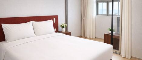 A hotel room with a large bed, a nightstand, a window with curtains, and a view of the cityscape.