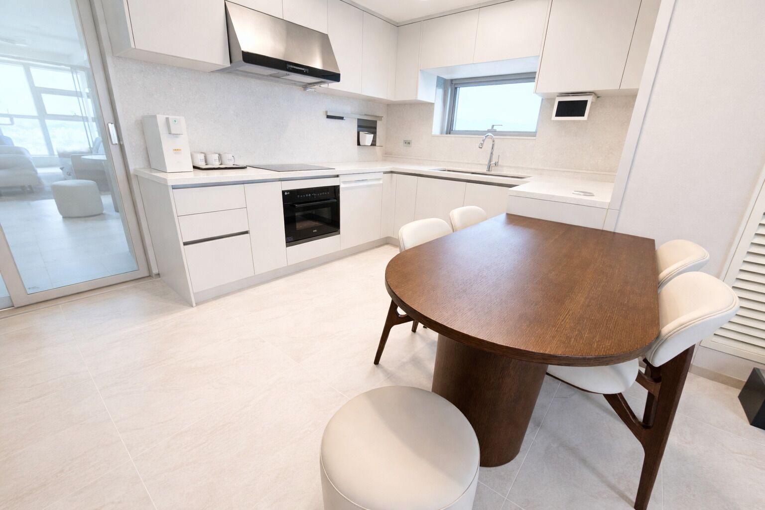 A modern kitchen with white cabinetry, a built-in oven, and a round dining table with chairs.