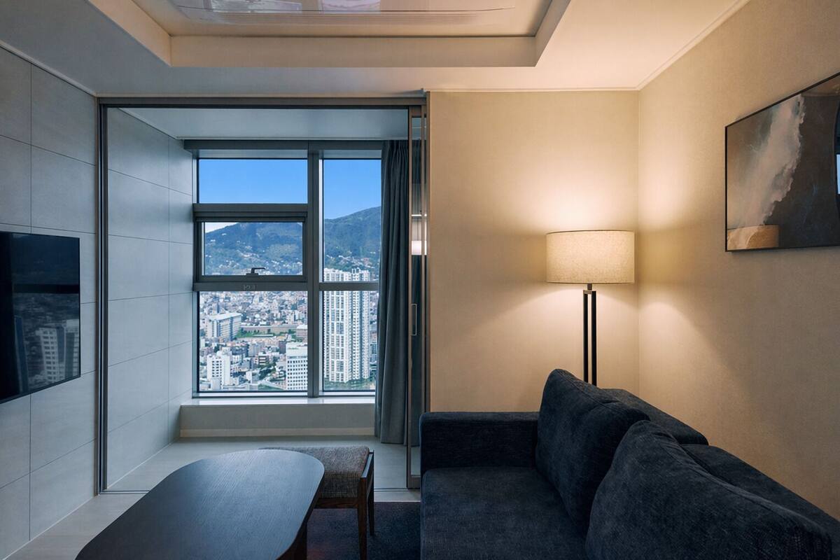 A modern room with a large window, a sofa, a table, and a floor lamp.