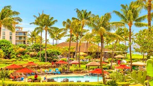 Un resort con zona de piscina, palmeras y un edificio con varios balcones.