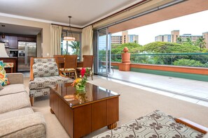 Una sala de estar moderna con un sofá, sillas, una mesa de centro y un balcón con vistas a edificios y zonas verdes.