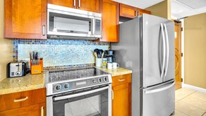 Una cocina con armarios de madera, un refrigerador de acero inoxidable, un microondas, una estufa y una cafetera.