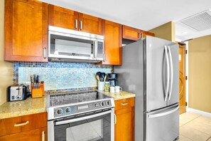 A kitchen with wooden cabinets, a stainless steel refrigerator, a microwave, a stove, and a coffee maker. - Honua Kai | Ocean View 7 BR, Sleeps 24 | Car Incl. w/ 6+ Nights | HKK ML-3269 by KBM (Lahaina)