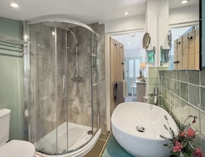 Een badkamer met een douche met glazen wand, een vrijstaand bad en een betegelde muur.