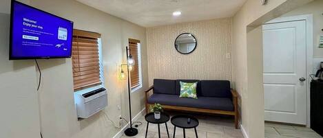 A living room with a sofa, two small tables, a television, and a wall-mounted mirror.