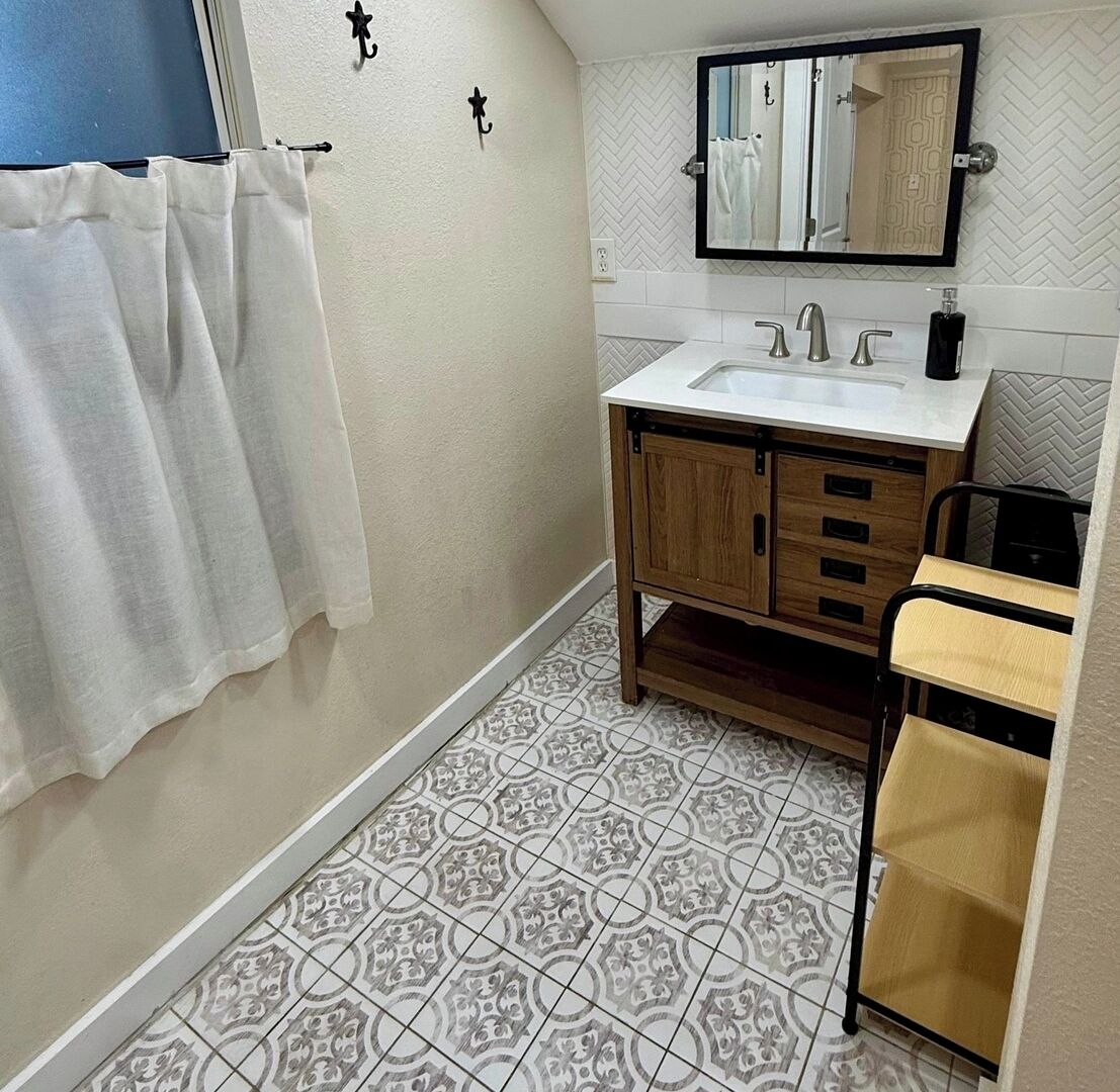 Un bagno con un lavandino bianco, mobili contenitori in legno, uno specchio e piastrelle a motivi decorativi.