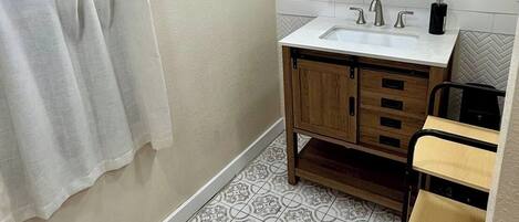 Un bagno con un lavandino bianco, mobili contenitori in legno, uno specchio e piastrelle a motivi decorativi.