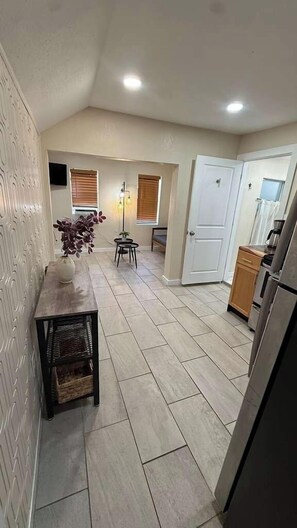 Un pasillo estrecho con una mesa de comedor, sillas, una planta pequeña y una puerta que da a una zona de cocina.