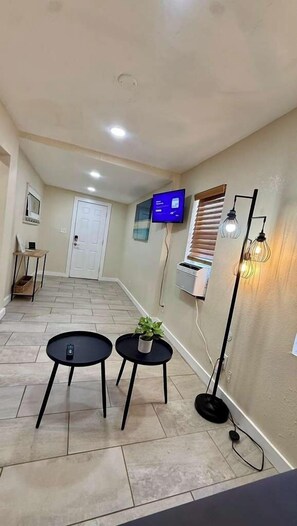 Un pasillo con un televisor de pantalla plana en la pared, una mesita con una planta y una lámpara de pie.