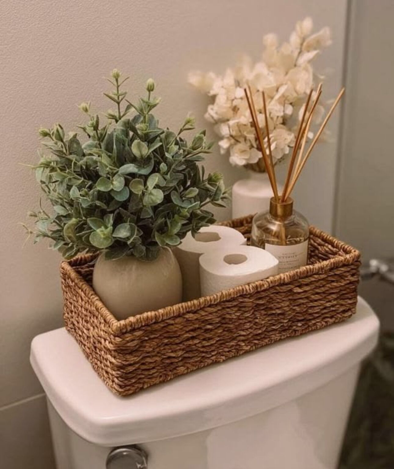 Ein Korbwäschesammler auf der Toilette mit einer Pflanze, einer Vase und einem Schilferoamper.