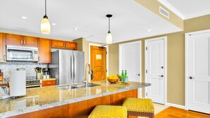 A kitchen with wooden cabinets, a stainless steel refrigerator, a microwave, and a granite countertop. - Honua Kai | Ocean View 7 BR, Sleeps 24 | Car Incl. w/ 6+ Nights | HKK ML-3287 by KBM (Lahaina)