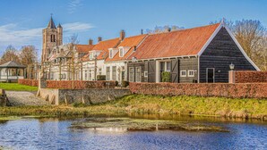 A historic building with a red-tiled roof, a stone tower, and a canal in front. - 2 bedroom lovely home in Heinkenszand (Heinkenszand)