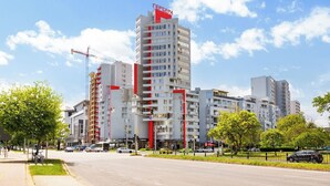 A multi-story hotel with a prominent red and white facade, located at a city intersection with visible traffic and greenery. - A2 Modern 1-bed Apartment 2 (Plovdiv)