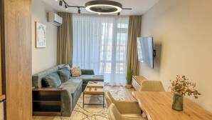 A modern living room with a sectional sofa, a wooden coffee table, a TV, and a dining area with a wooden table and chairs. - A2 Modern 1-bed Apartment 2 (Plovdiv)