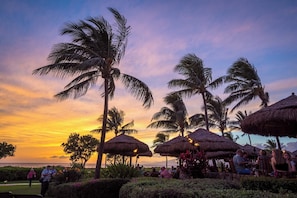 A sunset view with palm trees and thatched umbrellas, suggesting a tropical resort setting. - Honua Kai | Ocean View 4 BR, Sleeps 12 | Car Incl. w/ 6+ Nights | HKK ML-3305 by KBM (Lahaina)