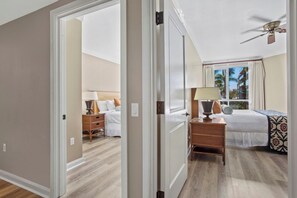 Ein Hotelzimmer mit Bett, Nachttisch, Lampe und Blick auf Palmen durch das Fenster.