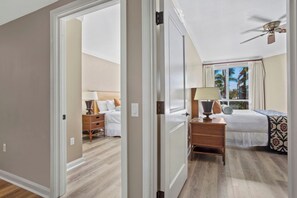 Une chambre d’hôtel avec un lit, une table de chevet, une lampe et une vue sur les palmiers par la fenêtre.