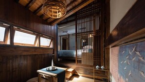 A traditional Japanese room with tatami flooring, a low table, a hanging light fixture, and a sliding door leading to another room.