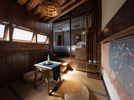 Una habitación japonesa tradicional con suelo de tatami, una mesa baja, una lámpara colgante y una puerta corredera que da a otra habitación.