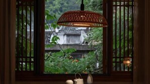 A traditional room with a window, a hanging lamp, a table with tea set, and a view of a wooden structure.