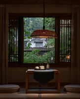 Habitación tradicional con ventana, lámpara colgante, una mesa con juego de té y vistas a una estructura de madera.
