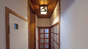 Ein schmaler Korridor mit Holzboden, einer Tür mit kleinem Fenster und einer traditionellen japanischen Schiebetür mit mattiertem Glas.