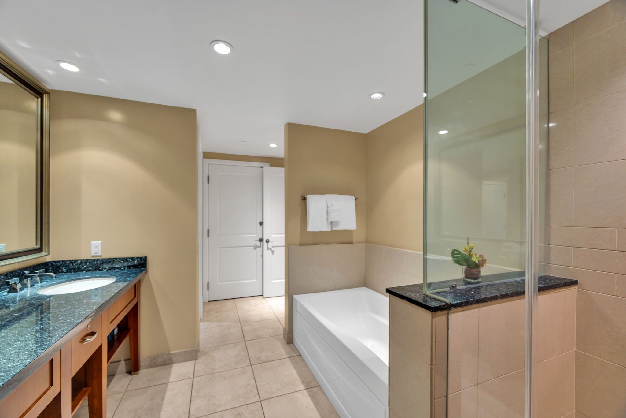 A modern bathroom with a large mirror, two sinks, a bathtub, and a shower.