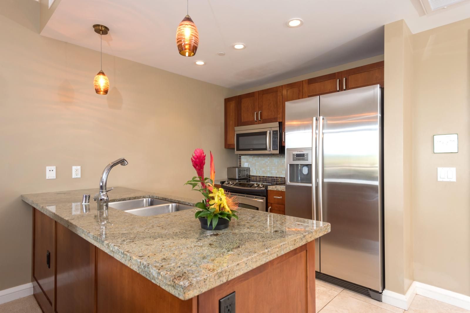 Una cocina con encimeras de granito, electrodomésticos de acero inoxidable, armarios de madera e iluminación colgante.