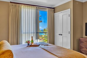 Ein Hotelzimmer mit Bett, einem Fenster mit Vorhängen, einer Tür und einem kleinen Tisch mit Flasche und Gläsern.