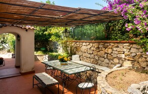 Un patio al aire libre con una mesa, sillas, un muro de piedra y una pérgola.