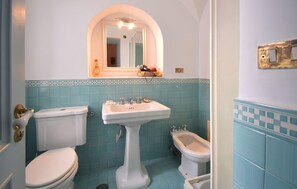 Un baño con inodoro, bidé y lavamanos, con azulejos azules y un espejo sobre el lavamanos.
