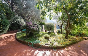 A garden with a brick pathway, a bird feeder, and various plants.