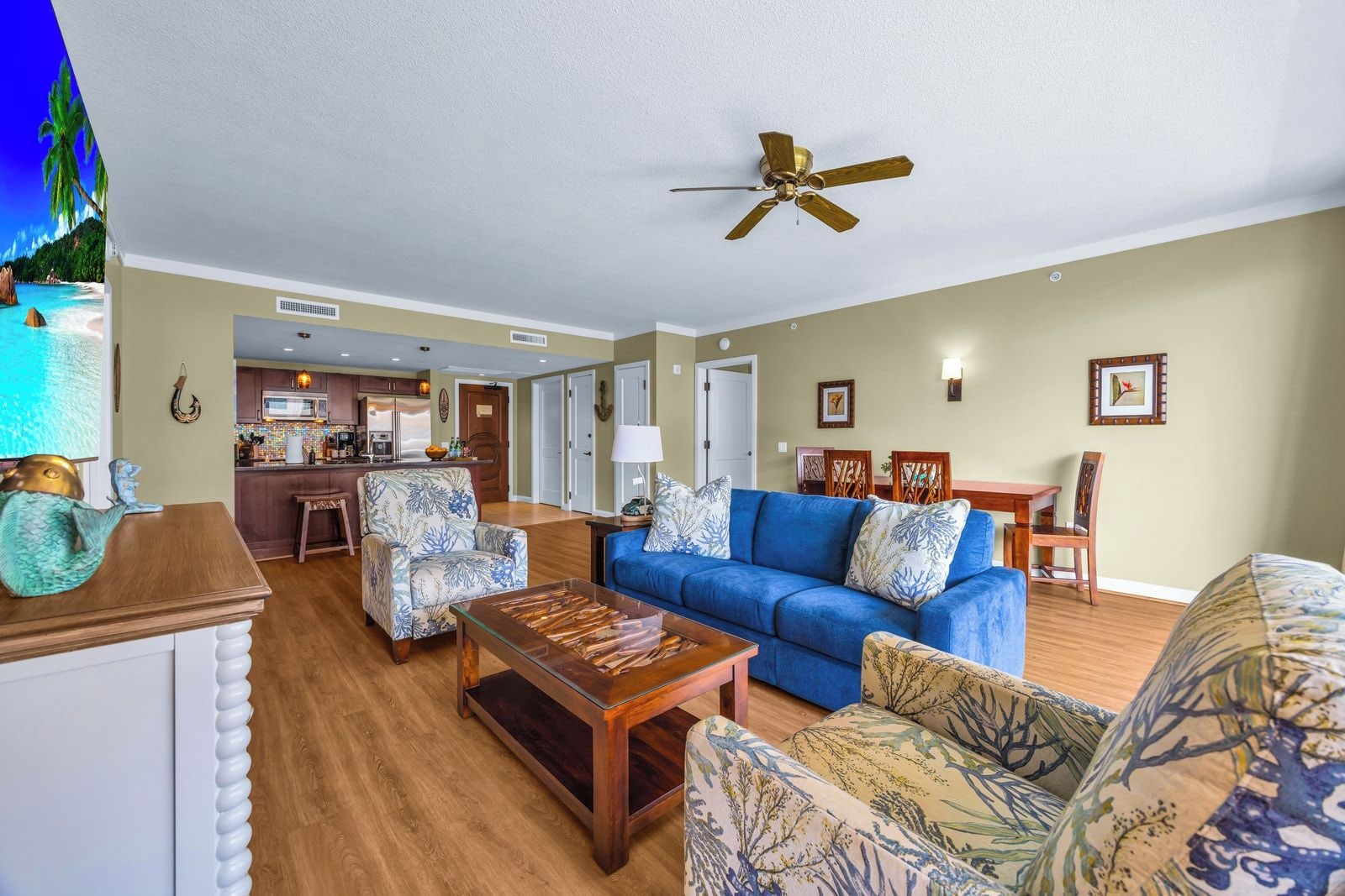 A living room with a blue sofa, patterned armchairs, a wooden coffee table, and a ceiling fan.