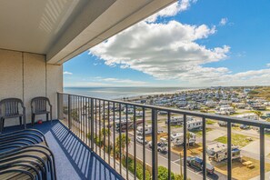 A balcony with chairs, a view of a parking lot with RVs, and a distant coastline.