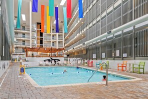An indoor swimming pool with a wooden deck, colorful flags, and a view of the building's interior.