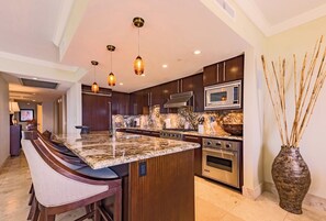 A modern kitchen with dark wood cabinets, a granite countertop, stainless steel appliances, and pendant lighting. - Honua Kai | Ocean View 8 BR, Sleeps 22 | Car Incl. w/ 6+ Nights | HKK ML-3377 by KBM (Lahaina)