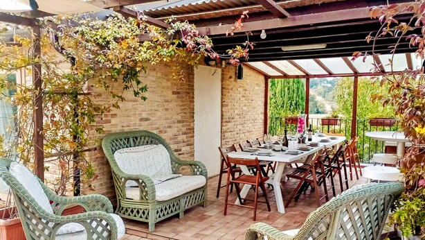 Un patio cubierto con mobiliario de mimbre, una mesa de comedor lista para seis personas y una pared de ladrillo.