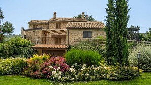 Una casa de piedra con techo de tejas, un balcón de madera y un jardín bien cuidado con diversas plantas y flores.
