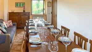 Un comedor con una mesa larga dispuesta para seis comensales, sillas, un sofá, un armario y un ventanal con vistas a zonas verdes.