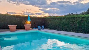 Piscina con vista al atardecer, rodeada de setos y plantas en macetas.