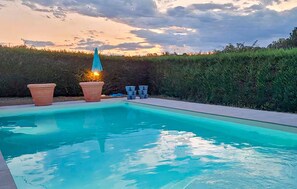 Ein Swimmingpool mit Sonnenuntergangsblick, umgeben von einer Hecke und Kübelpflanzen.