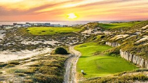 A golf course with a sandy path, green fairways, and a sunset in the background. - New 4BR Ocean View Villa with Airport Transport (Cabo San Lucas)