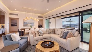 A modern living room with a sectional sofa, a coffee table, and a dining area with a view. - New 4BR Ocean View Villa with Airport Transport (Cabo San Lucas)