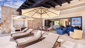 A sunlit outdoor lounge area with lounge chairs, a large umbrella, and a blue sofa set. - New 4BR Ocean View Villa with Airport Transport (Cabo San Lucas)