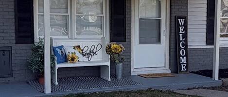 Una casa con porche, una banca, un letrero de bienvenida y un buzón.