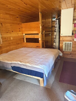 Una habitación de cabaña de madera con una cama, un calentador y una ventana con cortinas.